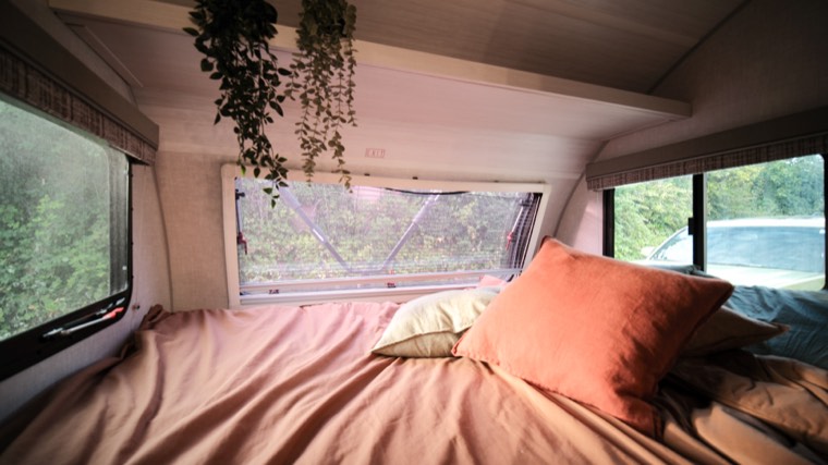 Rear bed made up with linens and a window looking out to the trees